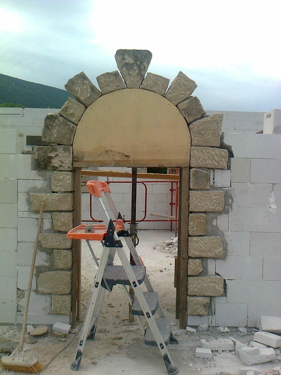 Stone arch built on its timber centring, in a wall still going up.