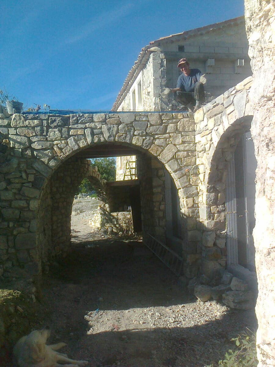 Vaulted stone passage, two arches in line, mason sitting on the wall being built.