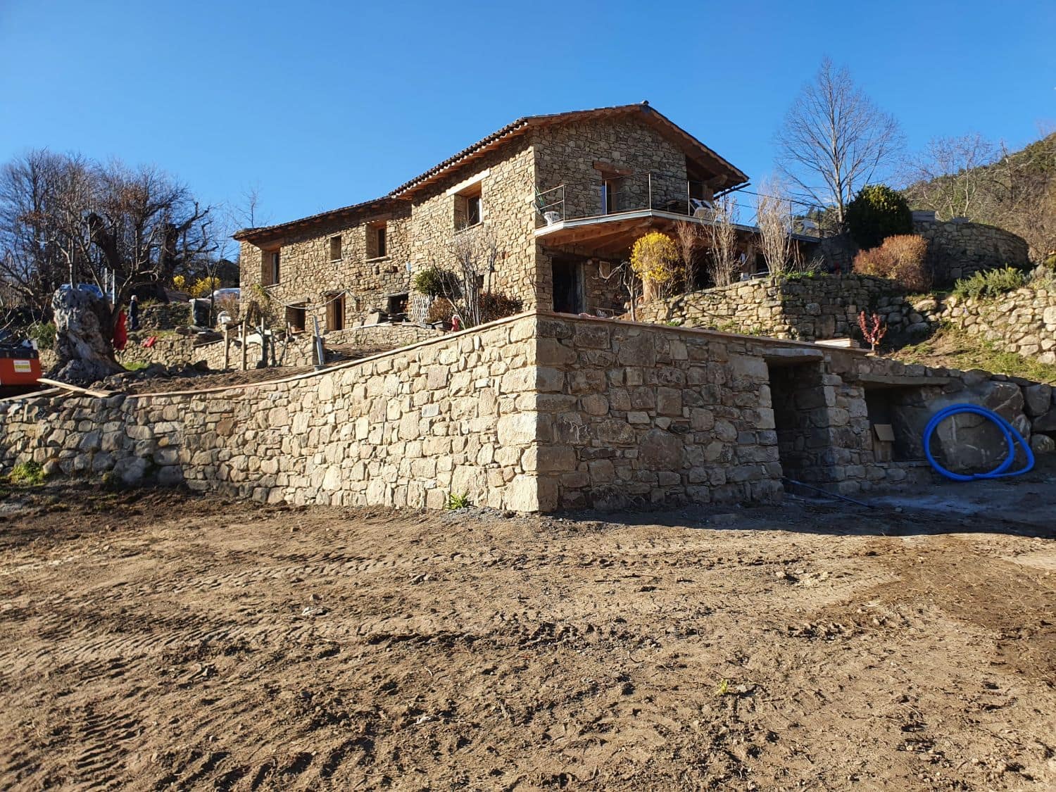 Stone building and its long curved retaining wall, ground still being worked.