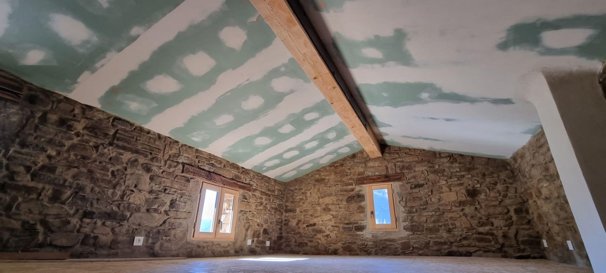 Interior room with bare stone walls, old timber lintels above the windows, new ceiling and exposed beam.