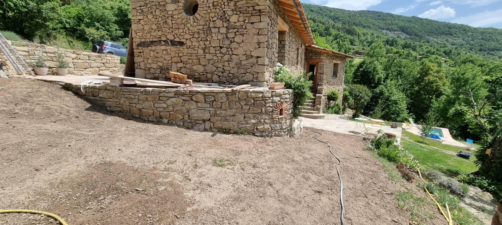 Curved dry-stone retaining wall carrying the terrace of the house, facing the wooded valley.
