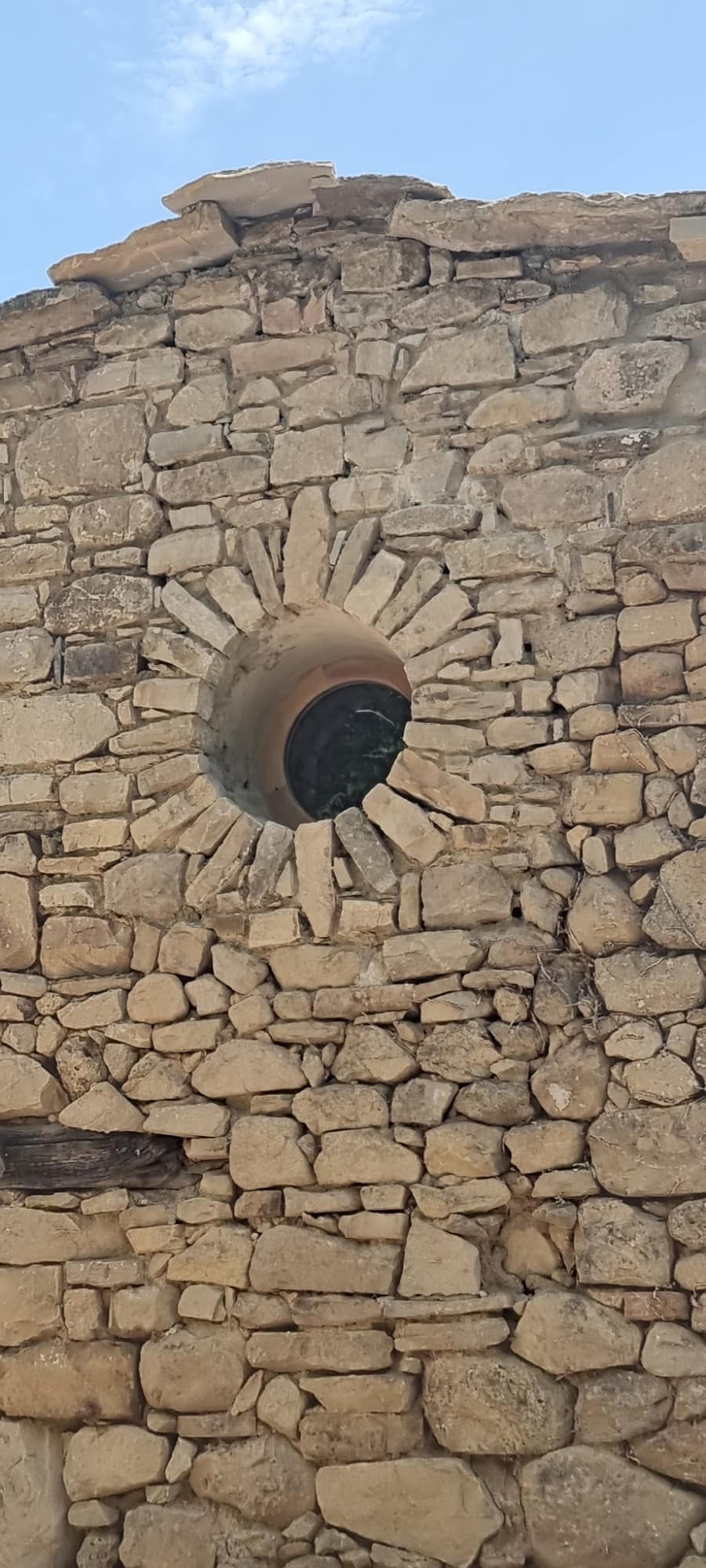 Round opening cut in a dry-stone gable, framed by stones set in a sunburst.