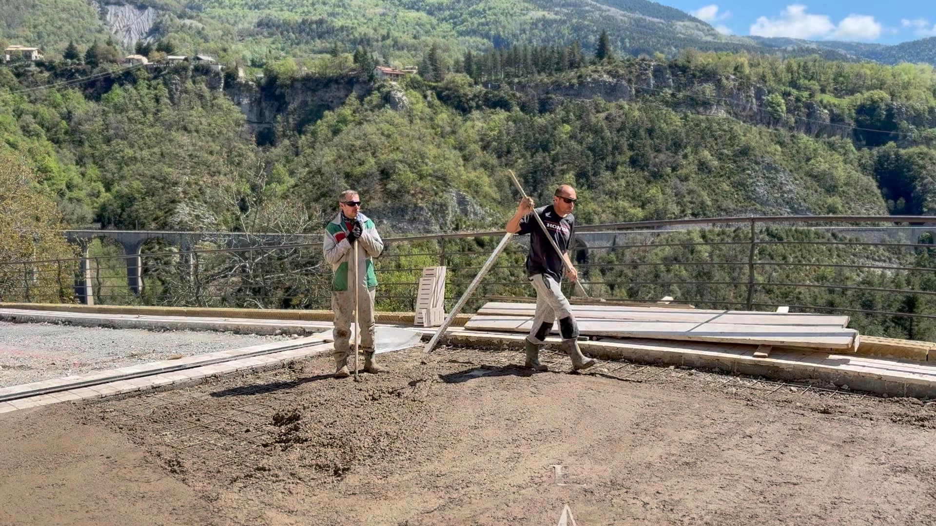 Two masons screeding a terrace slab, viaduct and valley behind them.