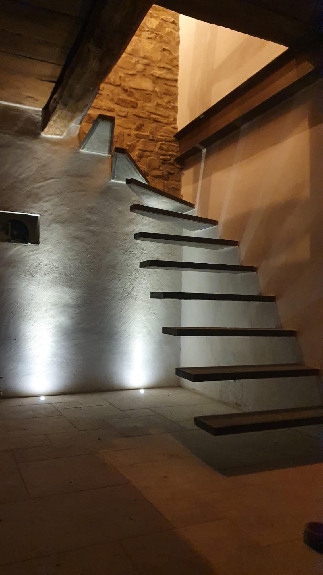 Cantilevered stair treads against a stone wall, with floor-level lighting.