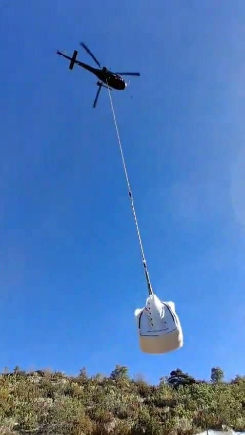 A helicopter sets down a bulk bag of materials on a mountain site, where no road goes up.