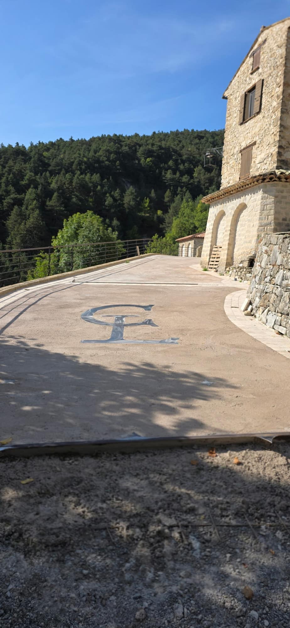 Monogram cast into the terrace slab, in front of the stone façade and its arches.