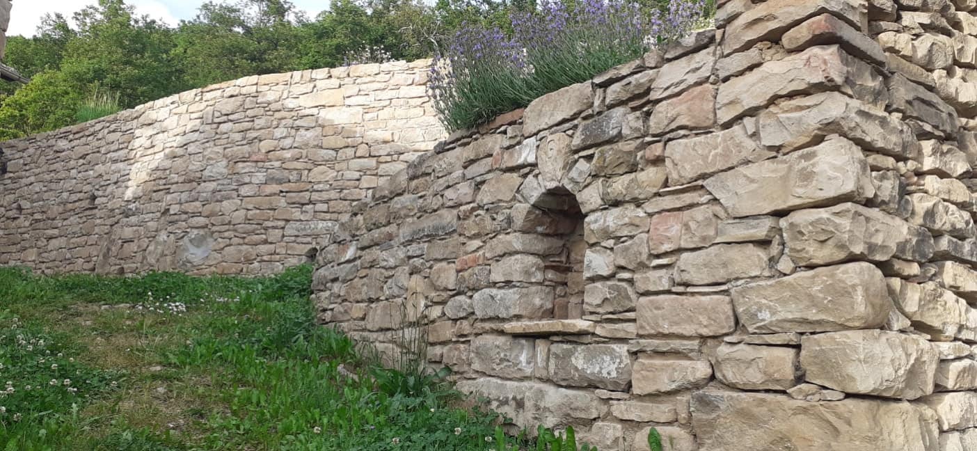 Dry-stone wall with a round-arched niche, lavender along the top.