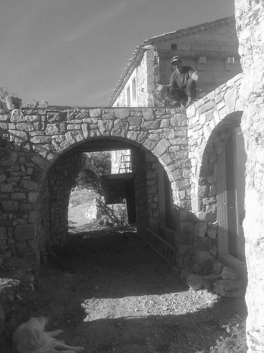 Passage voûté en pierre, les arcs montés un à un, un maçon assis sur le mur à l'étage.