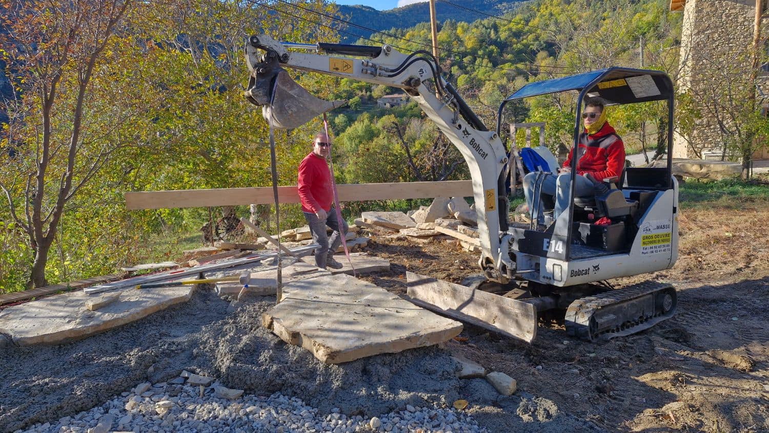 Laying large stone slabs with a mini-excavator, two SARL MASSE masons on site.