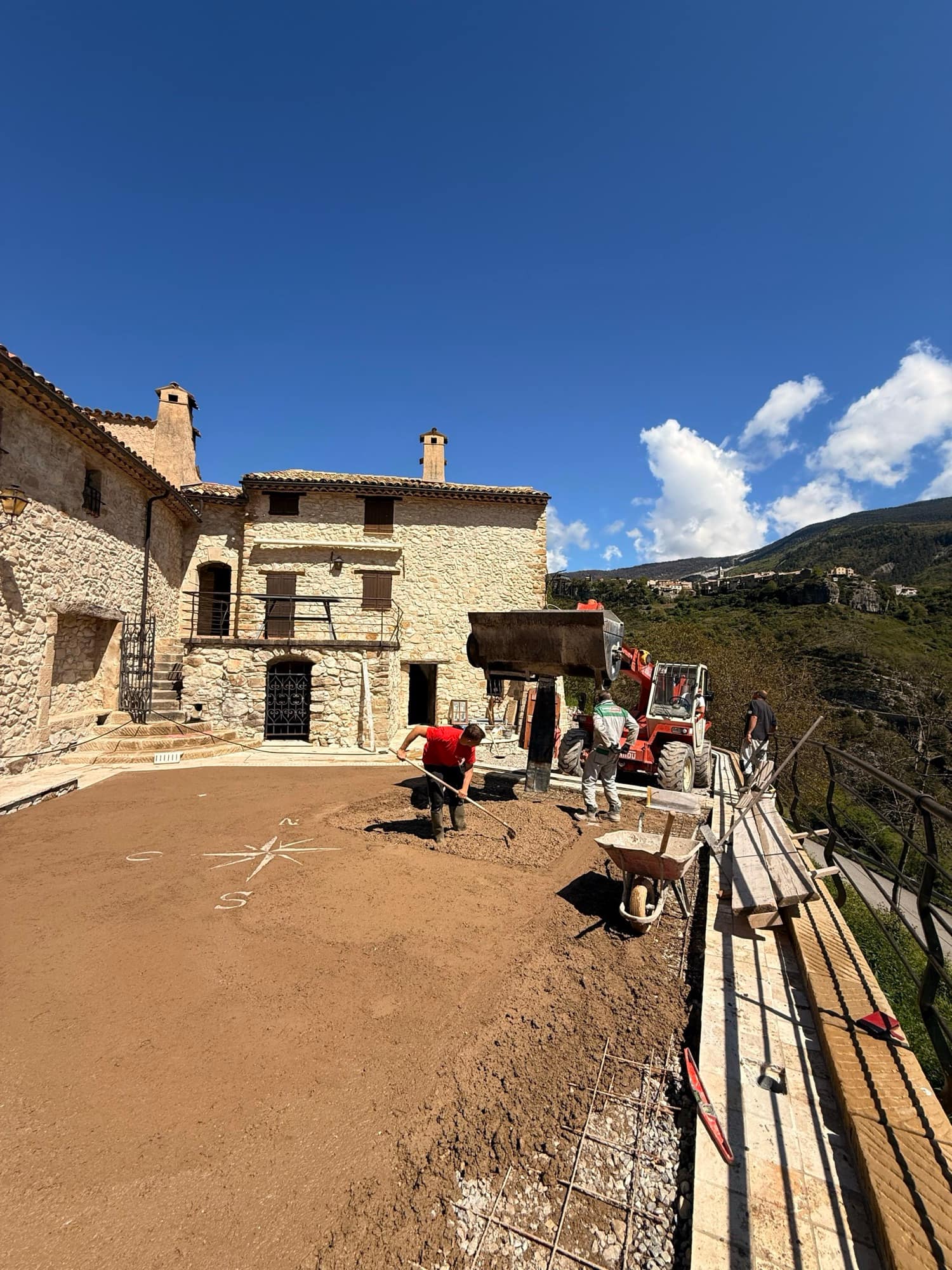 Stone bastide restored by SARL MASSE, terrace being finished, hilltop village and mountains behind.