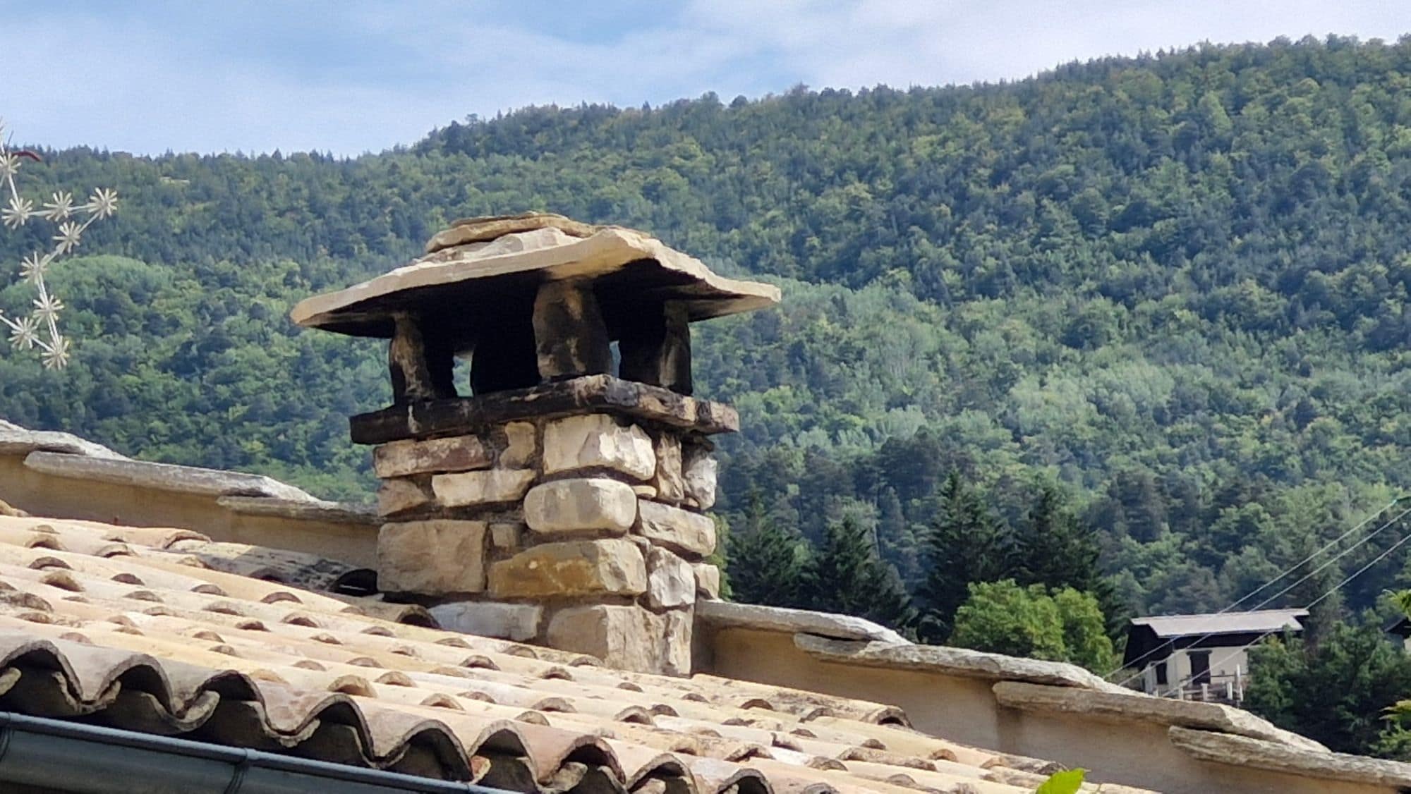 Stone chimney stack capped with stone slabs, above a canal tile roof.