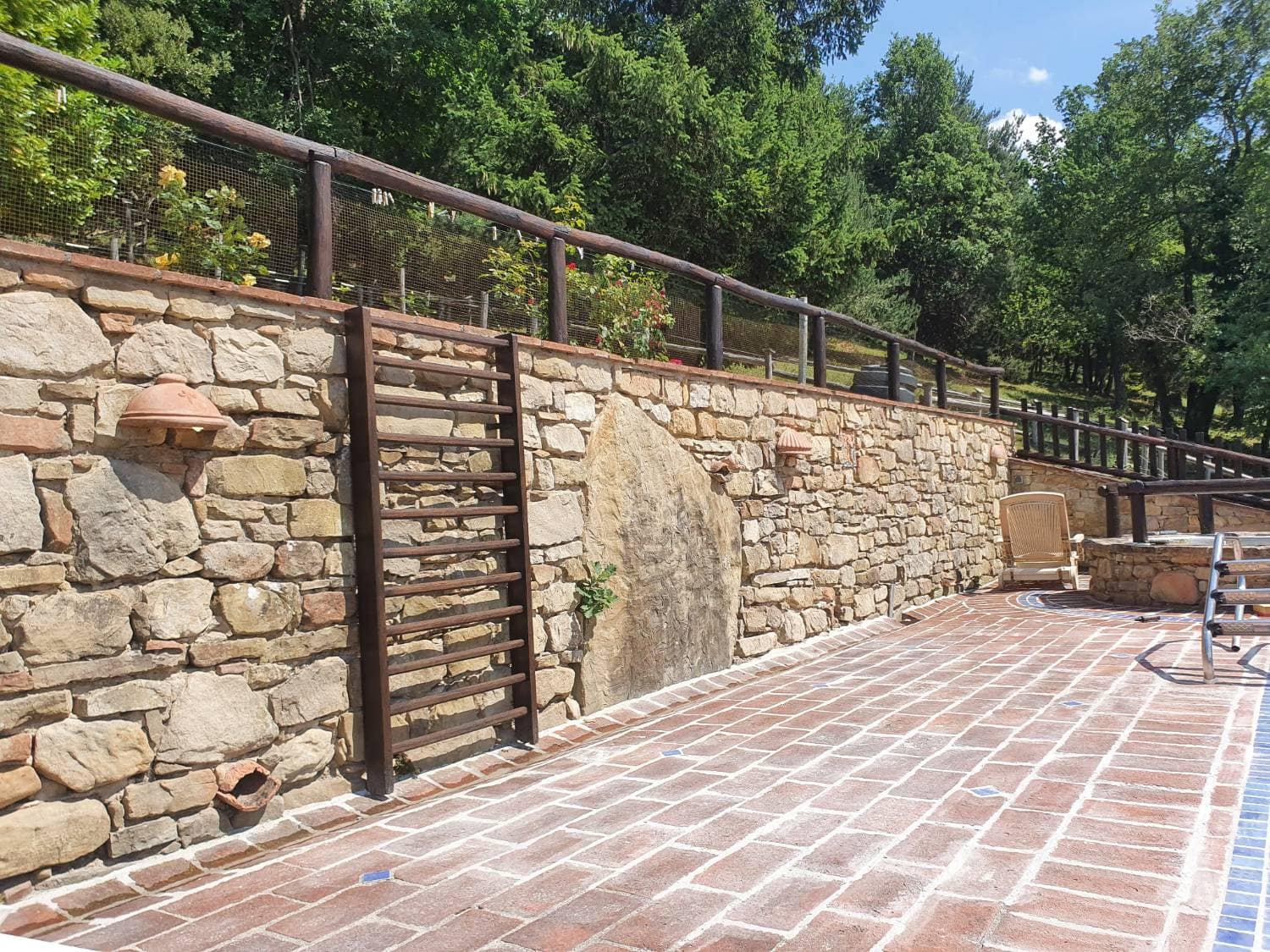 Terracotta terrace edged by a stone wall, with a timber handrail.