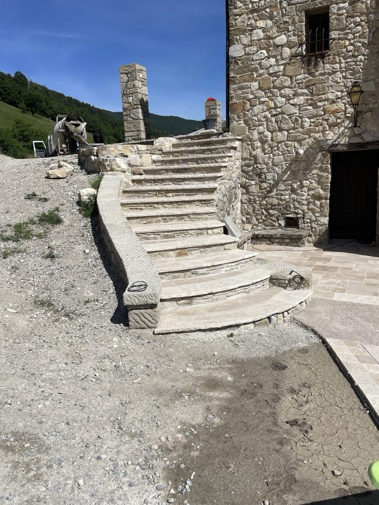 Outdoor staircase in cut stone, curved treads and a solid stringer, against a bare stone façade.