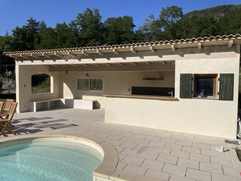 Rendered pool house under round tiles, exposed timber frame, at the edge of the pool.